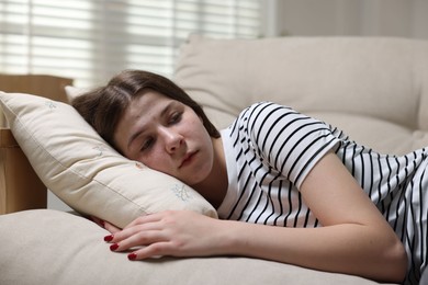 Photo of Depressed teenage girl lying on sofa at home