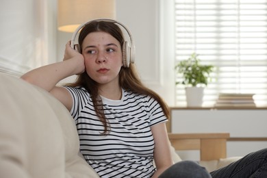 Photo of Upset teenage girl listening to music on sofa at home. Space for text