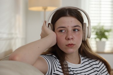 Photo of Upset teenage girl listening to music on sofa at home