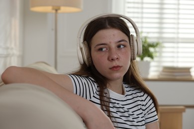 Photo of Upset teenage girl listening to music on sofa at home