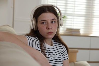 Photo of Upset teenage girl listening to music on sofa at home