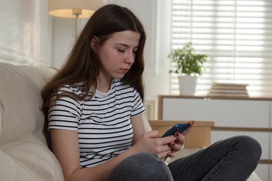 Photo of Upset teenage girl with smartphone on sofa at home. Space for text