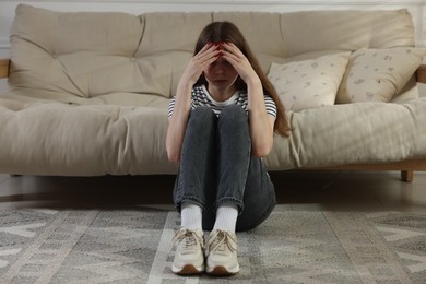 Photo of Depressed teenage girl on floor at home