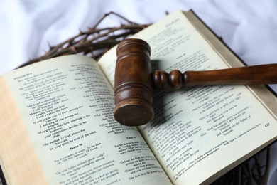 Photo of Judge's gavel, crown of thorns and Bible on white fabric, closeup