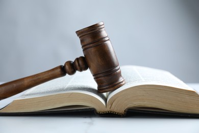 Photo of Judge's gavel and Bible on white marble table, closeup