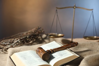 Photo of Judge's gavel, Bible, crown of thorns and scales on burlap fabric, closeup