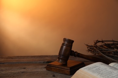 Photo of Judge's gavel, crown of thorns and Bible on wooden table against pale orange gradient background, closeup. Space for text
