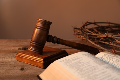Photo of Judge's gavel, crown of thorns and Bible on wooden table, closeup
