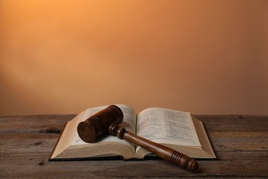 Photo of Judge's gavel and Bible on wooden table against pale orange background, closeup. Space for text