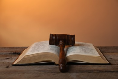 Photo of Judge's gavel and Bible on wooden table against pale orange background, closeup