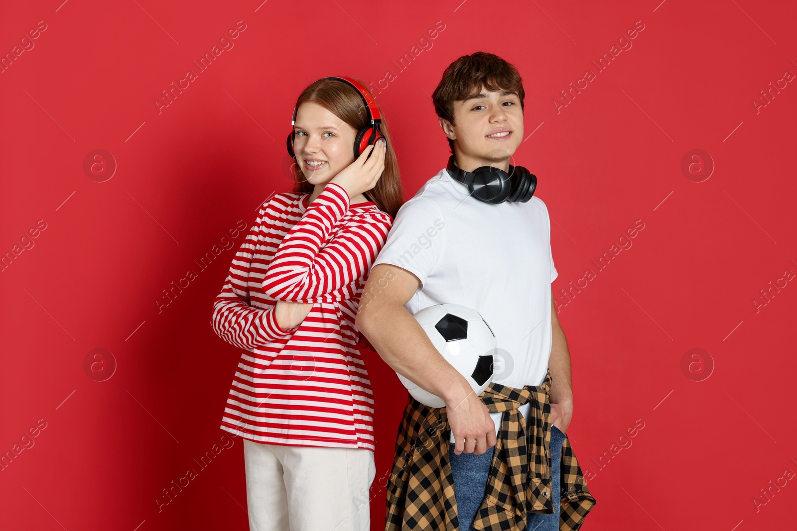 Teenagers with headphones and soccer ball on red background Photo of Teenagers with headphones and soccer ball on red background