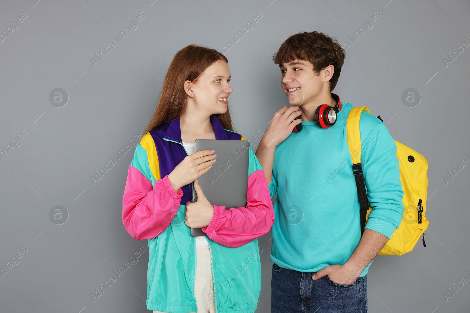 Teenagers with backpack and laptop on grey background Photo of Teenagers with backpack and laptop on grey background