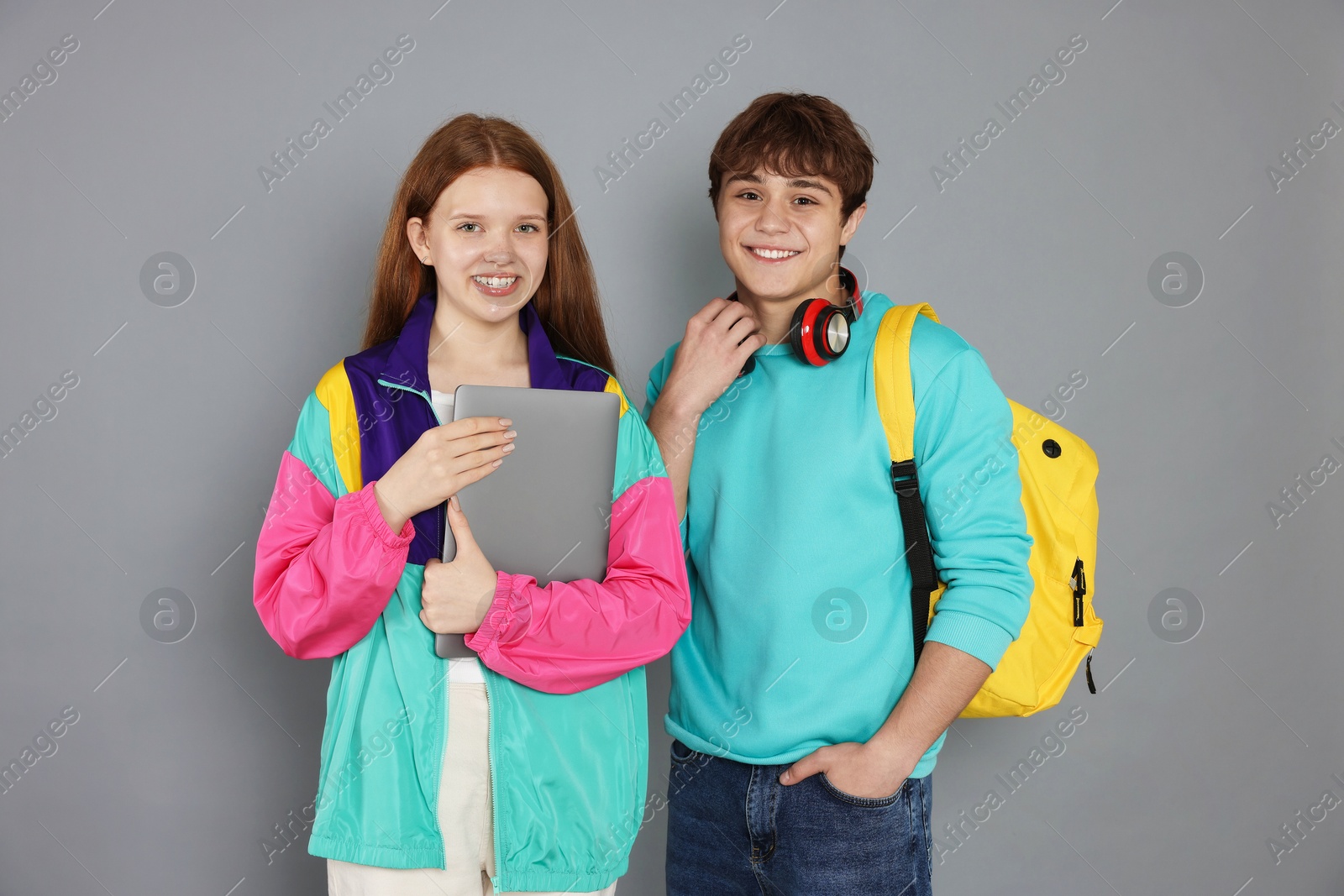 Teenagers with backpack and laptop on grey background Photo of Teenagers with backpack and laptop on grey background