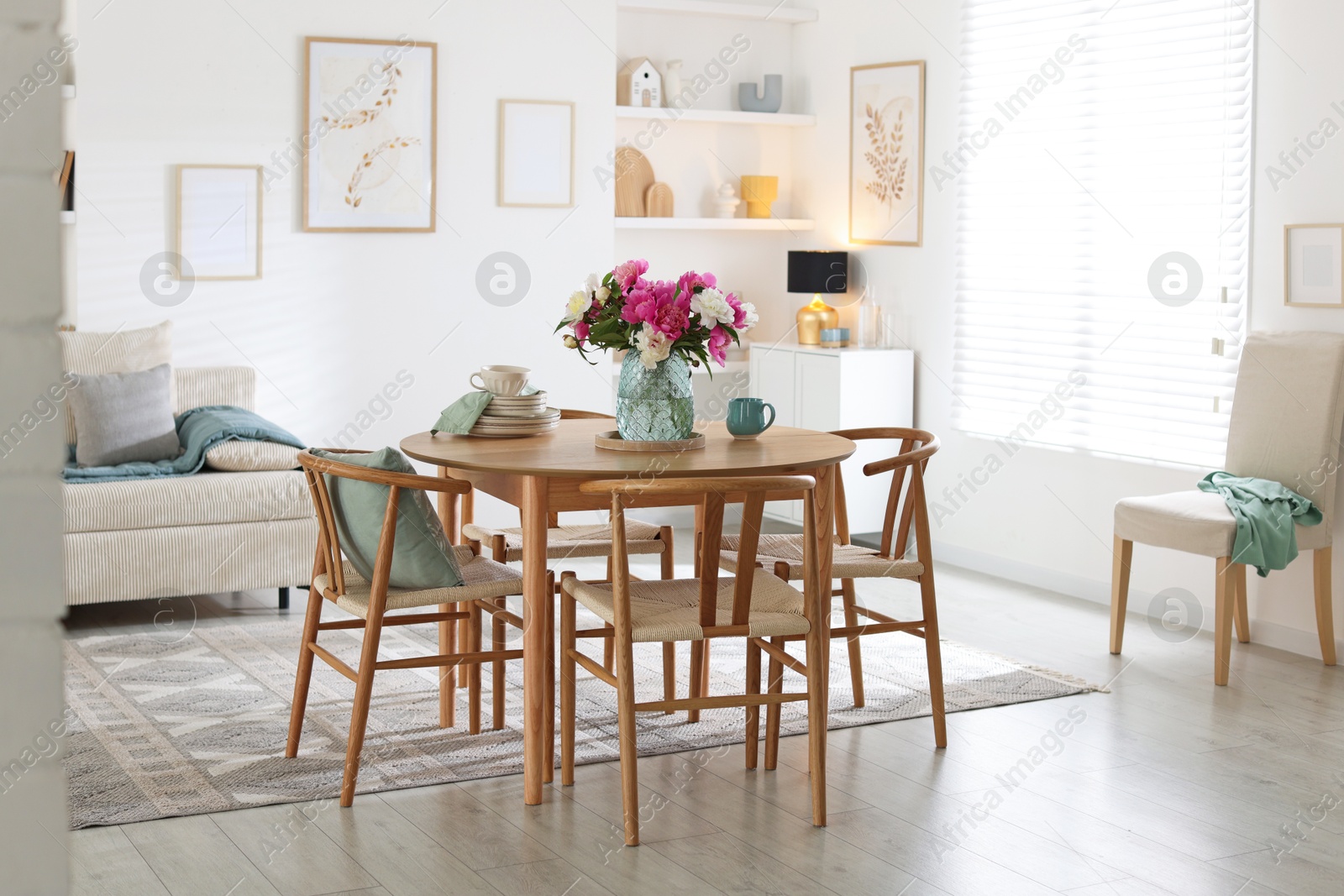 Dining table with beautiful flowers and dishware in room. Interior design Photo of Dining table with beautiful flowers and dishware in room. Interior design