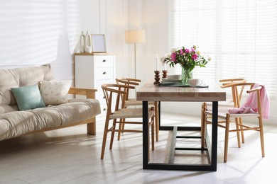 Photo of Dining table with beautiful flowers and dishware in room. Interior design