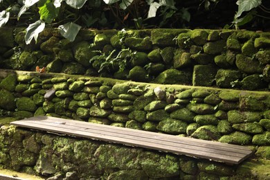 Photo of Wooden bench on rocky surface overgrown with moss in park
