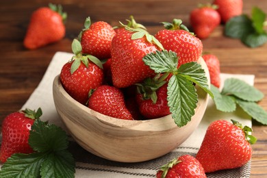 Photo of Fresh ripe strawberries and leaves in bowl on wooden table, closeup