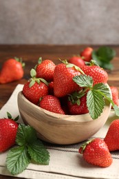 Photo of Fresh ripe strawberries and leaves in bowl on wooden table, closeup