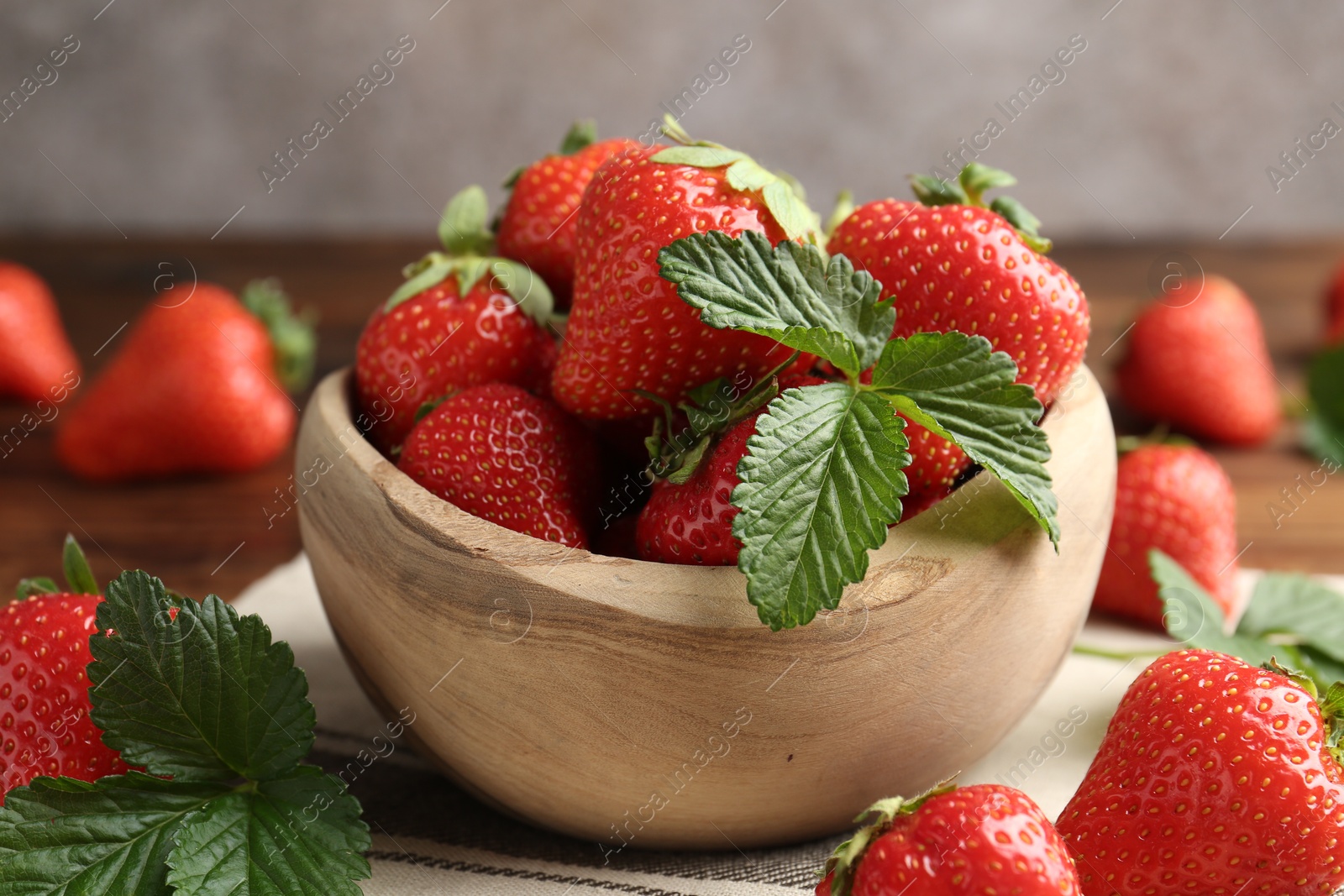 Fresh ripe strawberries and leaves in bowl on wooden table, closeup Photo of Fresh ripe strawberries and leaves in bowl on wooden table, closeup