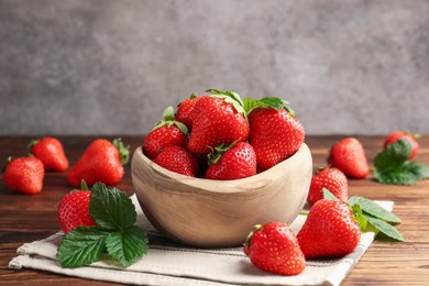 Photo of Fresh ripe strawberries and leaves in bowl on wooden table, closeup