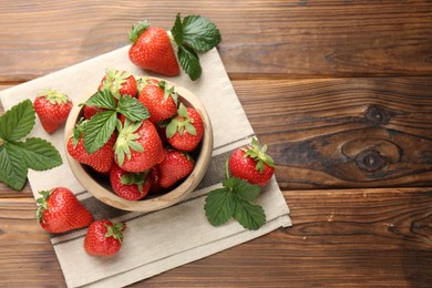 Photo of Fresh ripe strawberries and leaves in bowl on wooden table, flat lay. Space for text