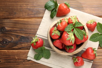 Photo of Fresh ripe strawberries and leaves in bowl on wooden table, flat lay. Space for text