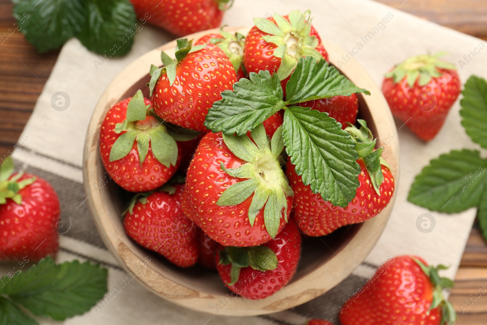 Fresh ripe strawberries and leaves in bowl on wooden table, flat lay Photo of Fresh ripe strawberries and leaves in bowl on wooden table, flat lay