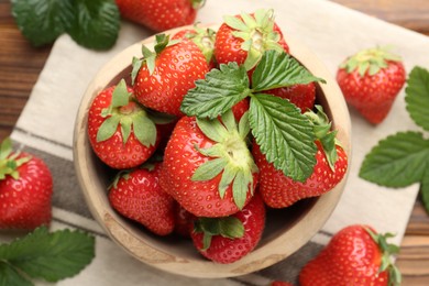 Photo of Fresh ripe strawberries and leaves in bowl on wooden table, flat lay