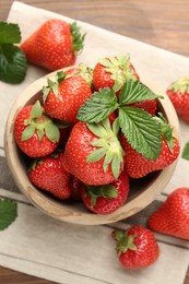 Photo of Fresh ripe strawberries and leaves in bowl on wooden table, flat lay