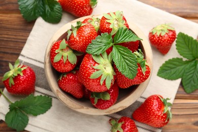 Photo of Fresh ripe strawberries and leaves in bowl on wooden table, flat lay