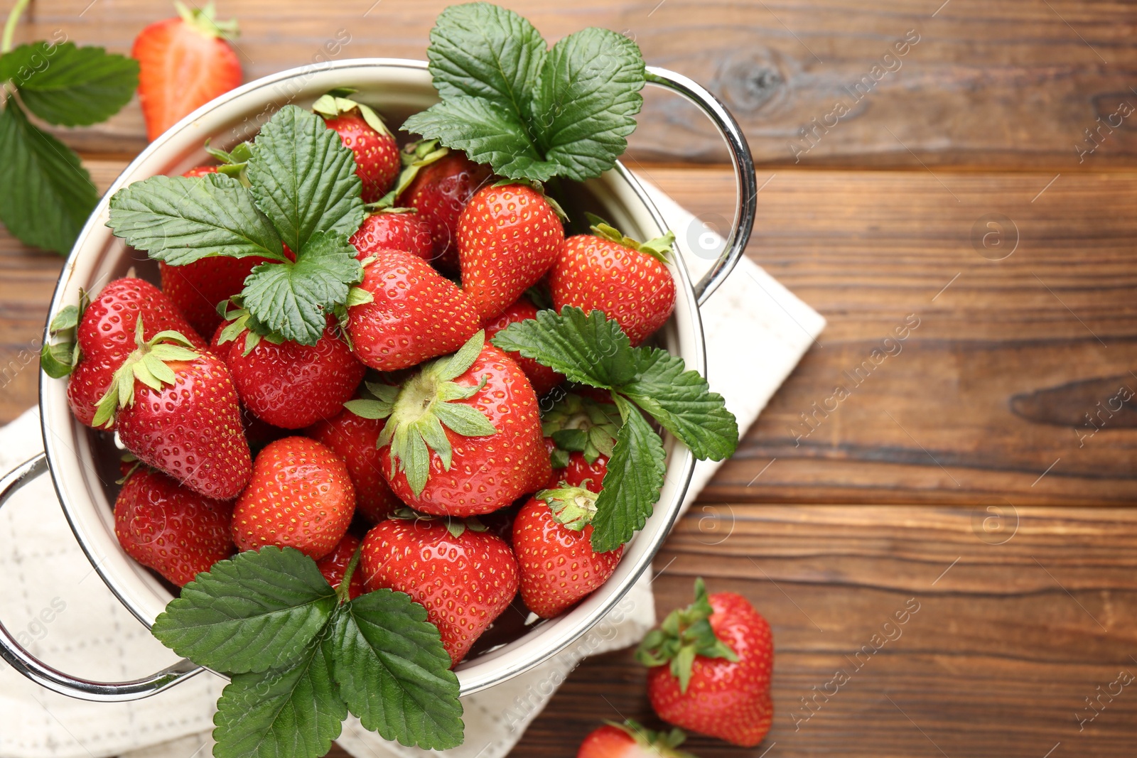 Fresh ripe strawberries and leaves in metal colander on wooden table, flat lay. Space for text Photo of Fresh ripe strawberries and leaves in metal colander on wooden table, flat lay. Space for text
