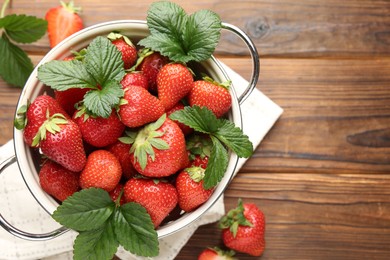 Photo of Fresh ripe strawberries and leaves in metal colander on wooden table, flat lay. Space for text