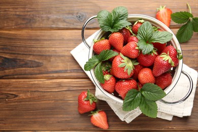Photo of Fresh ripe strawberries and leaves in metal colander on wooden table, flat lay. Space for text
