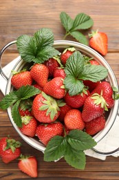 Photo of Fresh ripe strawberries and leaves in metal colander on wooden table, flat lay