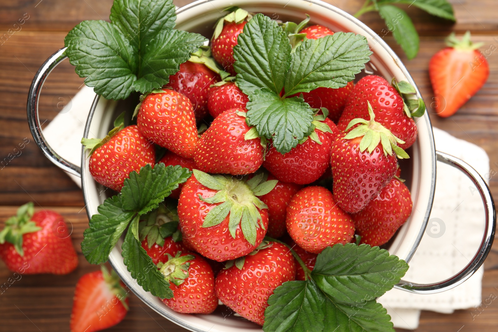 Fresh ripe strawberries and leaves in metal colander on wooden table, flat lay Photo of Fresh ripe strawberries and leaves in metal colander on wooden table, flat lay