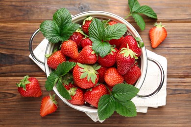 Photo of Fresh ripe strawberries and leaves in metal colander on wooden table, flat lay