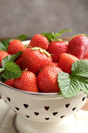 Photo of Fresh ripe strawberries and leaves in metal colander on table, closeup