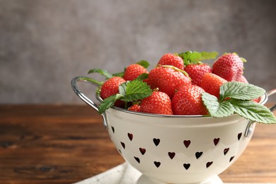 Photo of Fresh ripe strawberries and leaves in metal colander on wooden table, closeup. Space for text
