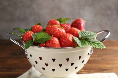 Photo of Fresh ripe strawberries and leaves in metal colander on wooden table, closeup