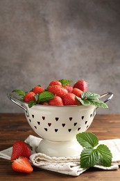 Photo of Fresh ripe strawberries and leaves in metal colander on wooden table