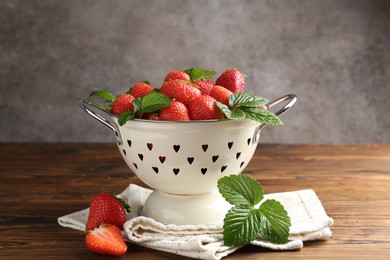 Photo of Fresh ripe strawberries and leaves in metal colander on wooden table