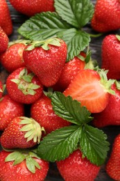 Photo of Fresh ripe strawberries and leaves on black wooden table, flat lay