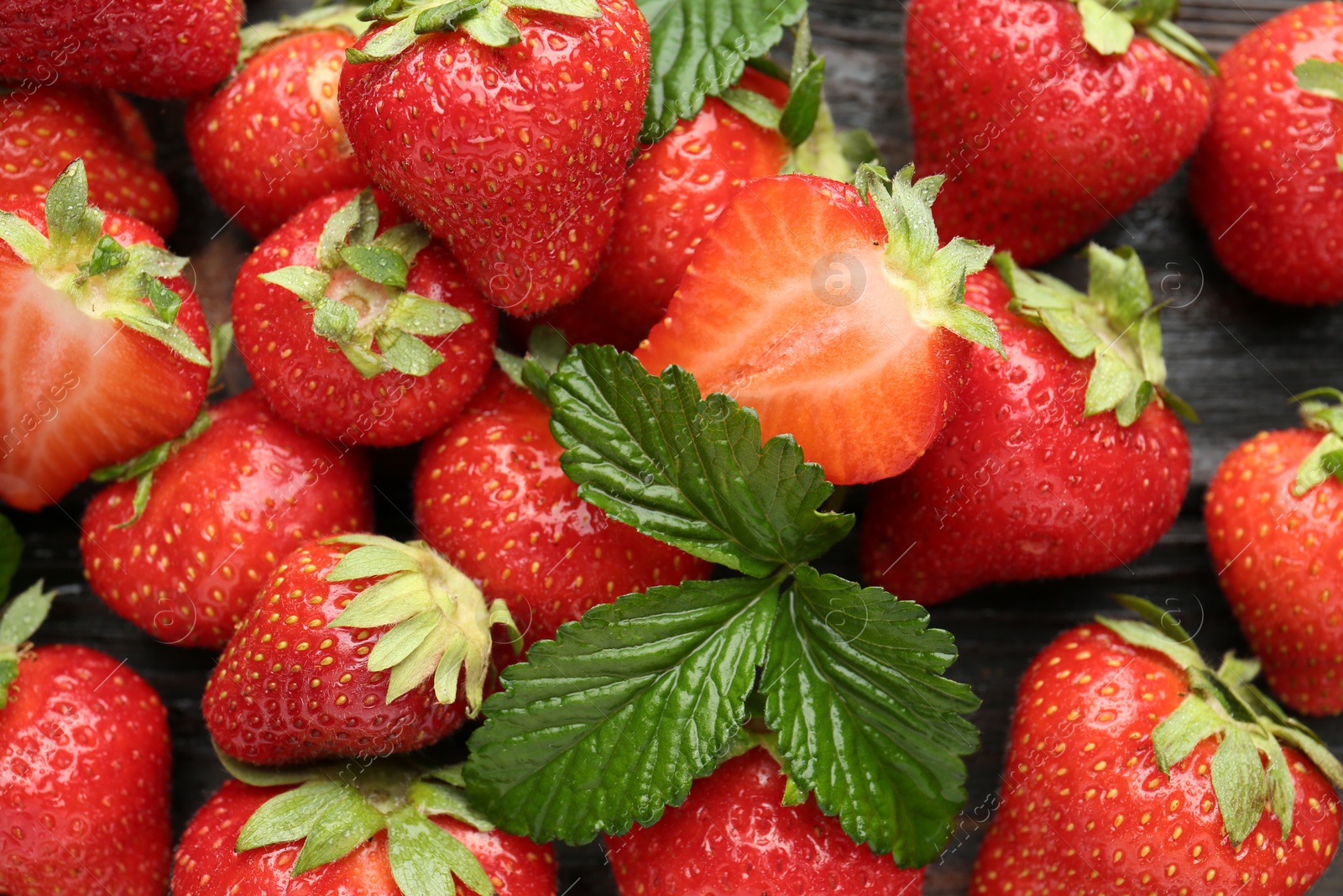 Fresh ripe strawberries and leaves on black wooden table, flat lay Photo of Fresh ripe strawberries and leaves on black wooden table, flat lay