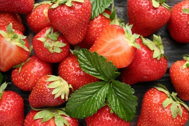 Photo of Fresh ripe strawberries and leaves on black wooden table, flat lay