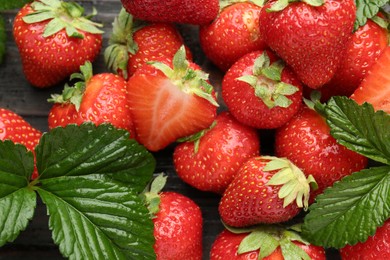 Photo of Fresh ripe strawberries and leaves on black wooden table, flat lay