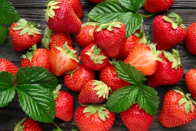 Photo of Fresh ripe strawberries and leaves on black wooden table, flat lay