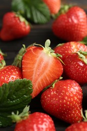 Photo of Fresh ripe strawberries and leaves on black wooden table, closeup