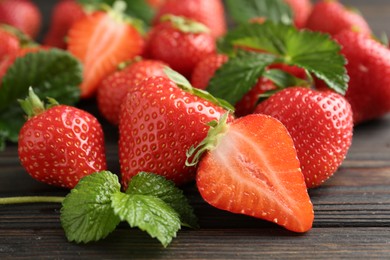 Photo of Fresh ripe strawberries and leaves on black wooden table, closeup