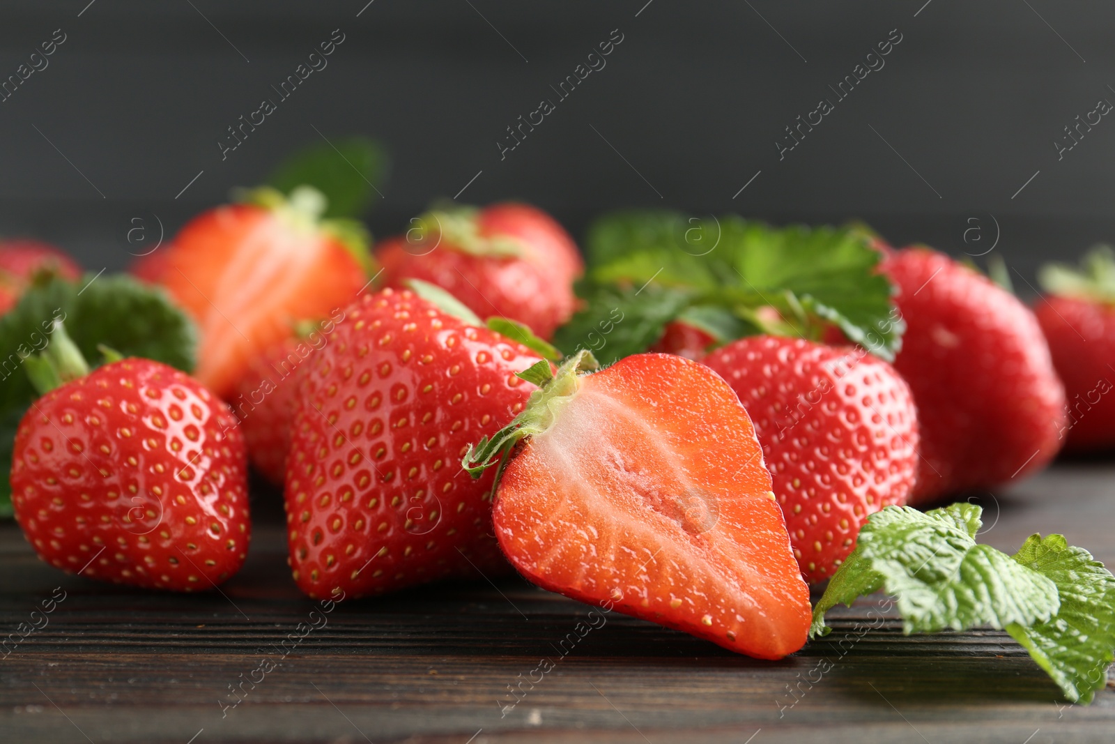 Fresh ripe strawberries and leaves on black wooden table, closeup Photo of Fresh ripe strawberries and leaves on black wooden table, closeup