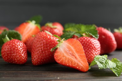Photo of Fresh ripe strawberries and leaves on black wooden table, closeup